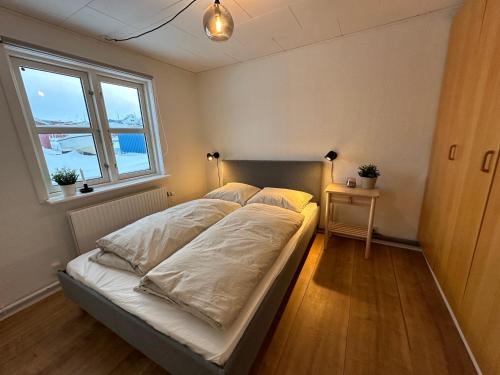 a bedroom with a bed with white sheets and a window at Det grønne hus med isbjergsudsigt in Ilulissat