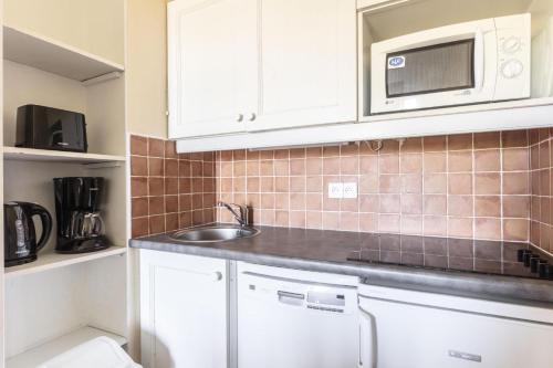 une cuisine avec des armoires blanches, un évier et un micro-ondes dans l'établissement Résidence Le Thabor - maeva Home - Appartement 2 Pièces 5 Personnes - Sélection MAE-9794, à Le Désert