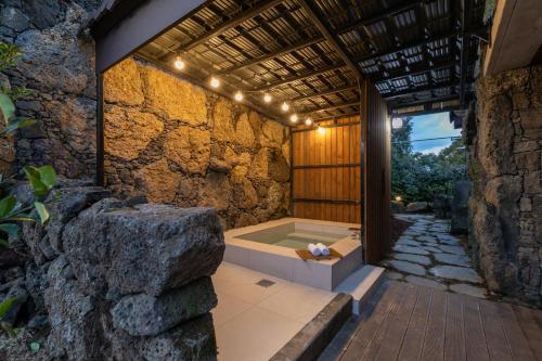 a bathroom with a tub in a stone wall at Bijarim Healing Pension in Jeju