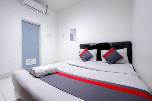een witte slaapkamer met een bed met rode en blauwe kussens bij J&B Rooms Tomang Jakarta Mitra RedDoorz in Jakarta