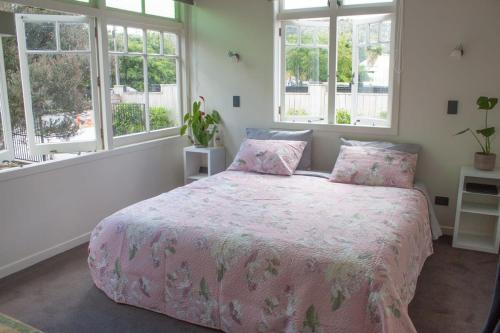 a bedroom with a pink bed with pillows and windows at Central Villa Oasis in Whangarei