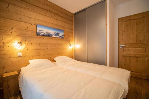a bedroom with a white bed with a wooden wall at Résidence LUMI BATIMENT B - Appartement LUMI B 814 in Valmorel