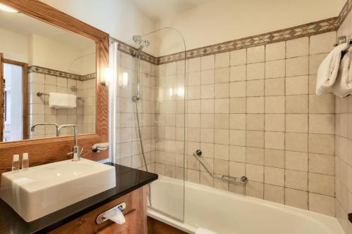 La salle de bains est pourvue d'un lavabo, d'une baignoire et d'un miroir. dans l'établissement Résidence Les Arcs Le Village - maeva Home - Appartement pièces - Prestige 204, à Bourg-Saint-Maurice