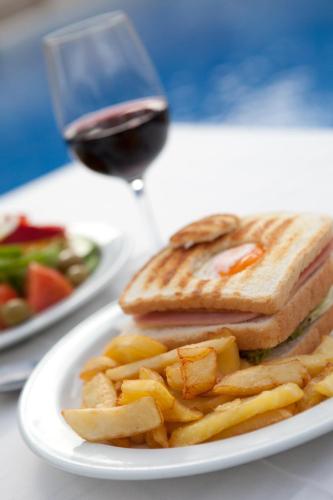 a sandwich and french fries on a plate with a glass of wine at Hotel-Apartamentos Andorra in Playa de las Americas