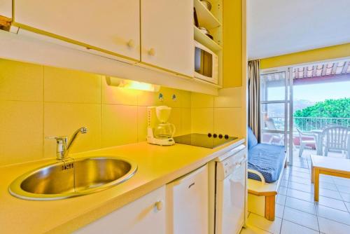 Il dispose d'un balcon et d'une cuisine jaune avec un évier. dans l'établissement Résidence le Hameau de Cap Esterel - maeva Home - Appartement 2 Pièces 5 Pe 11, à Saint-Raphaël