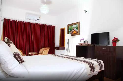 une chambre d'hôtel avec un lit blanc et un rideau rouge dans l'établissement Bharatham Heritage Inn, à Kannur