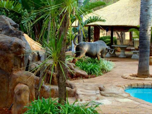 an elephant standing in a garden next to a pool at Kettle Guest Lodge Rustenburg in Rustenburg