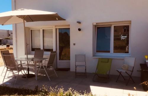 un patio con mesa, sillas y sombrilla en Dunes et Mer, en Plage Sainte-Cécile