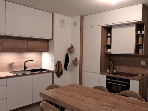 une cuisine avec des placards blancs et une table en bois avec des chaises dans l'établissement Appartement cosy 2 chambres - 300m de la plage, à Biscarrosse