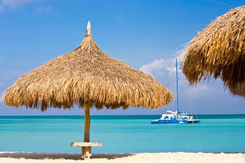 a straw umbrella on a beach with a boat in the water at Hyatt Regency Aruba Resort & Casino in Palm-Eagle Beach