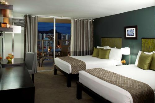 a hotel room with two beds and a balcony at Skyline Island Colony Hotel in Honolulu