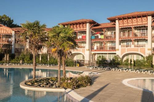 un grand bâtiment avec des palmiers en face d'une piscine dans l'établissement Résidence Le Domaine de Gascogne - maeva Home - Appartement 2 pièces 5 personnes Confort MAE-4457, à Biscarrosse