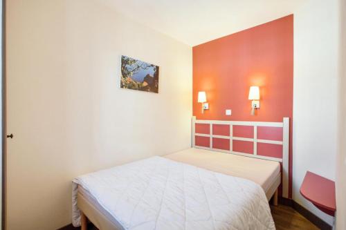 une chambre avec un lit blanc et un mur rouge dans l'établissement Résidence le Village de Cap Esterel - maeva Home - Appartement 2 pièces 5 personnes Sélection MAE-1255, à Saint-Raphaël