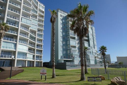 a large building with palm trees in front of it at Beach Club Unit 207 in Mossel Bay
