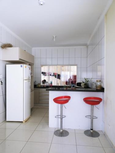 cocina con nevera blanca y 2 taburetes rojos en Casa da Pri, en São João Batista do Glória