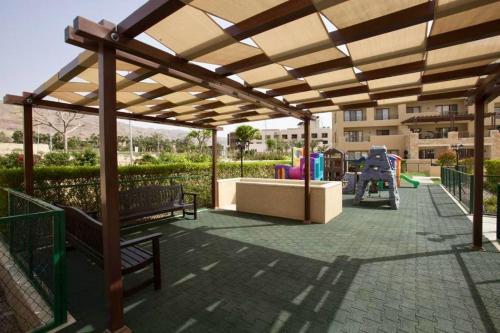 Apartment F14 - Samarah Resort في السويمة: جناح مع كراسي وملعب في حديقة