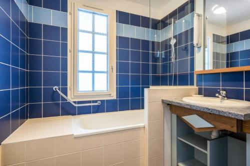 La salle de bains est pourvue de carrelage bleu, d'une baignoire et d'un lavabo. dans l'établissement Le Cap Glénan - maeva Home - Appartement 2 Pièces 4 Personnes - Confort 43, à Bénodet