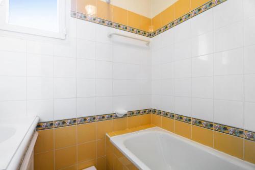 La salle de bains est pourvue d'une baignoire et de carrelage jaune et blanc. dans l'établissement Les Appartements aux Restanques du Golfe de St Tropez - maeva Home - Appartement duplex 3 Pièces 6 Personnes - Confort - vue Mer MAE-7771, à Grimaud