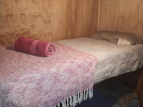 Cama en habitación de madera con almohada roja en Cabañas del mar, en Maitencillo