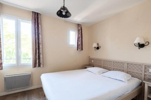 um quarto com uma cama branca e 2 janelas em Les Coteaux de Pont Royal en Provence - maeva Home - Maison 3 Pièces 6 Perso 13 em Mallemort