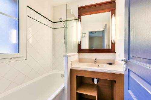 une salle de bain avec un lavabo, une baignoire et un miroir dans l'établissement Les Maisons de Lacanau les Pins - maeva Home - Maison 3 pièces 6 personnes - Sélection MAE-6658, à Lacanau