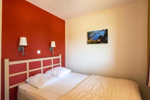 Ce lit se trouve dans une chambre dotée d'un mur rouge. dans l'établissement Résidence le Village de Cap Esterel - maeva Home - Appartement 2 Pièces 4 Personnes - Sélection MAE-7735, à Saint-Raphaël