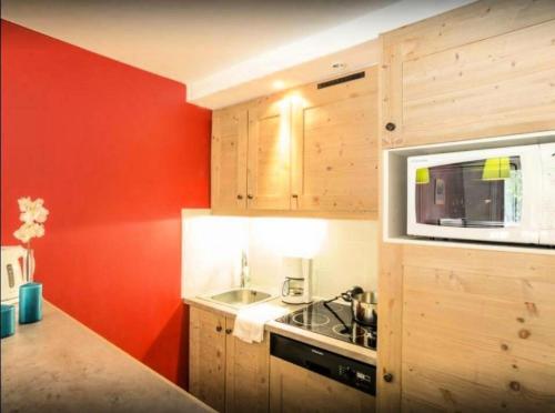 - une cuisine avec des murs rouges, une cuisinière et un four micro-ondes dans l'établissement Résidence Le Christiana - maeva Home - Appartement 2 Pièces 5 Personnes - Sélection MAE-7836, à Saint-Bon-Tarentaise