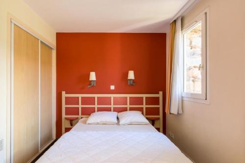 une chambre avec un lit avec un mur orange dans l'établissement Résidence le Village de Cap Esterel - maeva Home - Appartement 2 Pièces 6 Personnes - Sélection MAE-8258, à Saint-Raphaël
