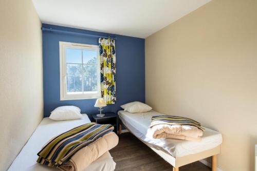 Cette chambre comprend 2 lits dans une chambre dotée de murs bleus et d'une fenêtre. dans l'établissement Les Maisons de Lacanau les Pins - maeva Home - Maison 3 pièces 6 personnes - Sélection MAE-8602, à Lacanau