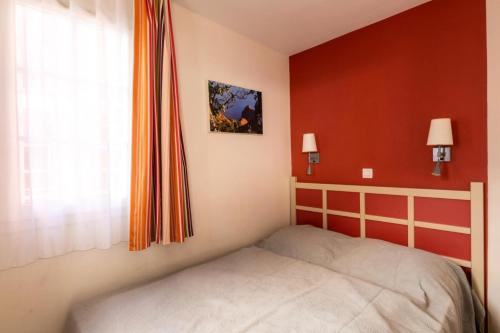 um quarto com uma cama e uma parede vermelha em Résidence le Village de Cap Esterel - maeva Home - Appartement 2 Pièces 5 P 43 em Saint-Raphaël