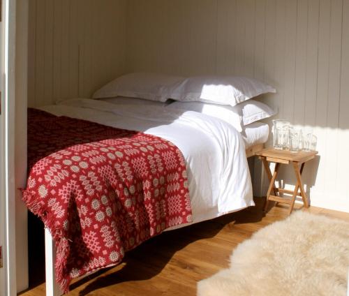 a bed with a red and white blanket and a table at Snowdonia Shepherds' Huts in Conwy