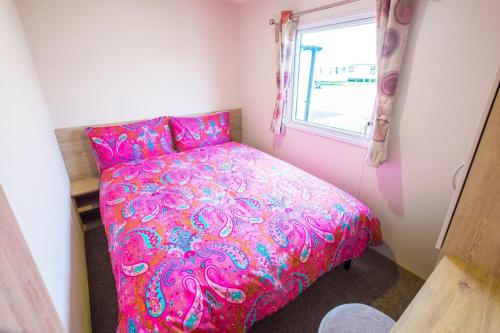 a pink bed in a small room with a window at SP158 - Camber Sands Holiday Park - 3 Bedrooms - Second Toilet - Decking - Private Parking in Camber