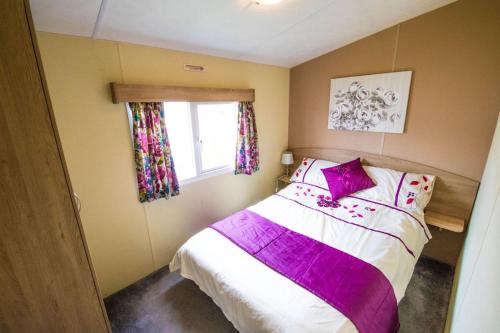 een slaapkamer met een bed met paarse lakens en een raam bij SBL70 - Camber Sands Holiday Park - Sleeps 8 - Close swimming pools and facilities - Private Parking in Camber