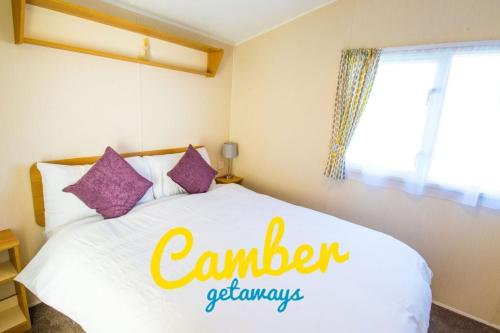 a bedroom with a white bed with purple pillows at SP90 - Camber Sands Holiday Park - Dog Friendly in Camber