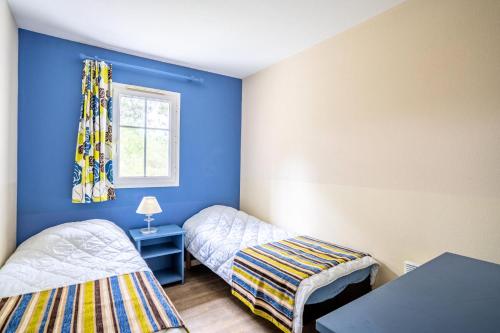 Cette chambre bleue comprend 2 lits et une fenêtre. dans l'établissement Les Maisons de Lacanau les Pins - maeva Home - Maison 3 Pièces 4 Personnes - Sélection MAE-2364, à Lacanau