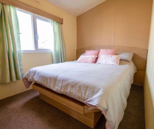 a bedroom with a bed with pink pillows and a window at MP252 - Camber Sands Holiday Park - Central Spot in Camber