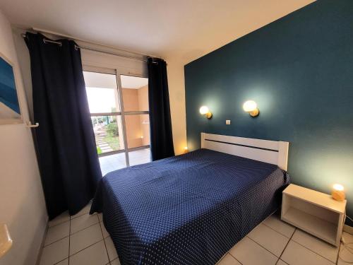 Un dormitorio con una cama azul y una ventana en Résidence le Hameau de Cap Esterel - maeva Home - Appartement 2 pièces 4 p 454, en Saint-Raphaël