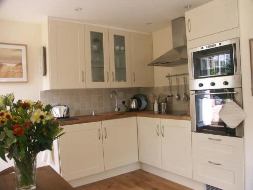 una cocina con armarios blancos y un jarrón de flores en The Gazebo in Winchelsea, en Winchelsea