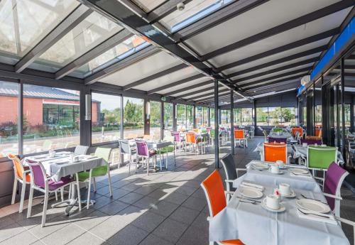 um restaurante com mesas, cadeiras e janelas em B&B HOTEL Colmar Liberté 4 étoiles em Colmar