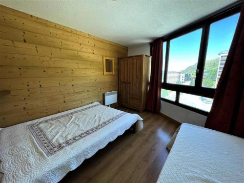 een slaapkamer met een houten muur, een bed en ramen bij Résidence Grande Masse - 2 Pièces pour 5 Personnes 894 in Les Menuires
