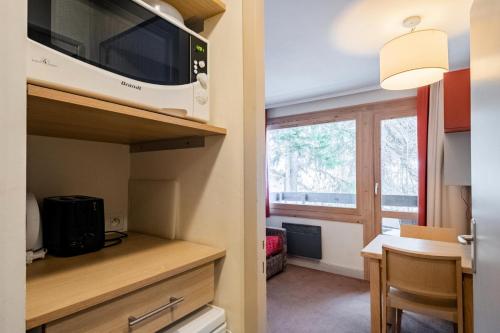 une petite cuisine avec un micro-ondes et une table dans l'établissement Résidence Plagne Lauze - maeva Home - Studio 2 Personnes - Confort MAE-0154, à Mâcot La Plagne