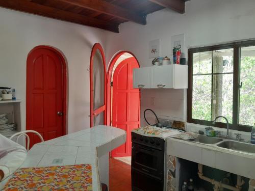 cocina con puertas rojas, fregadero y encimera en Cabañita Doña Tina, en Los Altos de Cerro Azul