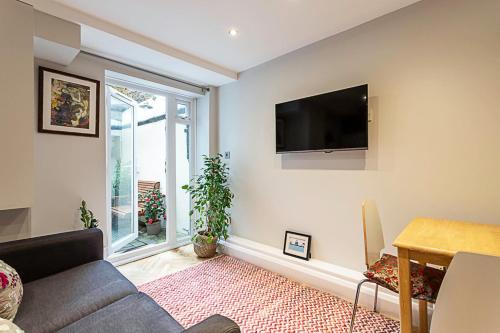 a living room with a couch and a tv on the wall at Cosy Garden Flat in Prestigious Residential Area in London