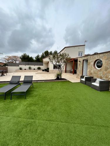 a green yard with benches and a building at Acogedora casa con piscina y 3 dormitorios in Vilanova i la Geltrú