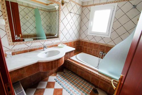 a bathroom with a sink and a tub and a mirror at Villa Romanza Beta in Agios Stefanos
