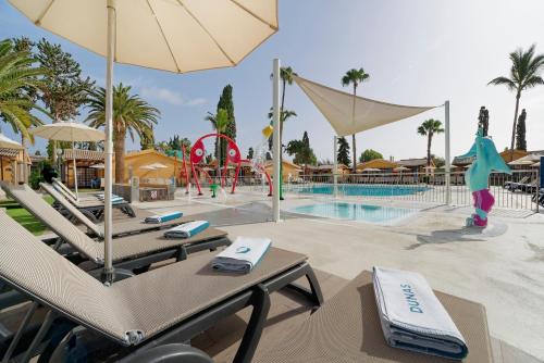 un complejo con piscina con sillas y sombrilla en Suites & Villas by Dunas en Maspalomas