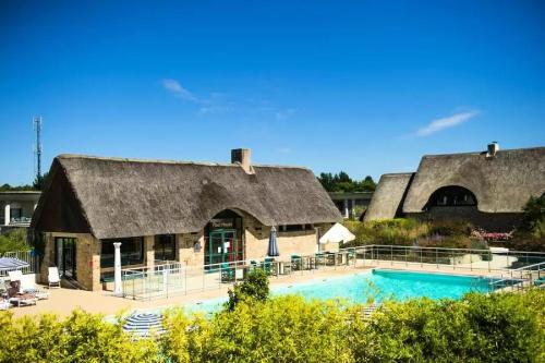 une maison avec un toit de chaume et une piscine dans l'établissement Résidence Le Saint Denac - maeva Home - Appartement 2 pièces 4 personnes - Prestige MAE-4234, à Saint-André-des-Eaux