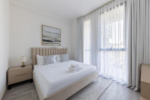 a white bedroom with a bed and a large window at Fresh & Quiet 1BR at Midtown Noor 4 Tower in Dubai