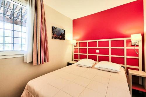 - une chambre dotée d'un lit avec un mur rouge dans l'établissement Résidence le Village de Cap Esterel - maeva Home - Appartement 2 pièces 6 personnes - Sélection MAE-0631, à Saint-Raphaël