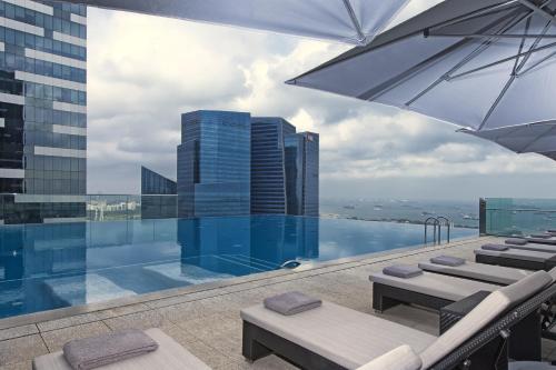 una piscina con sillas y una sombrilla en un edificio en The Westin Singapore en Singapur